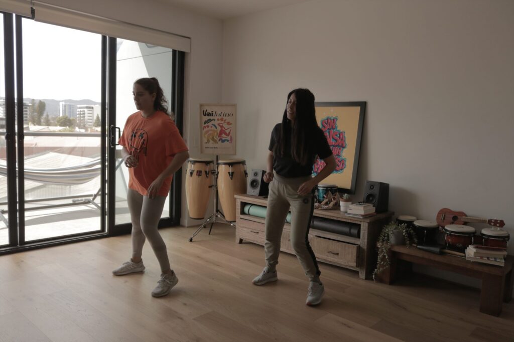 Two dancers practising steps side by side in a bright room